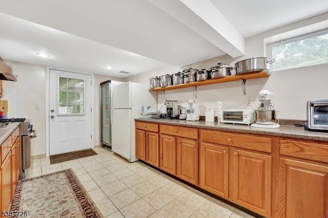 kitchen with white refrigerator, stainless steel range with gas stovetop, light tile patterned floors, and a wealth of natural light