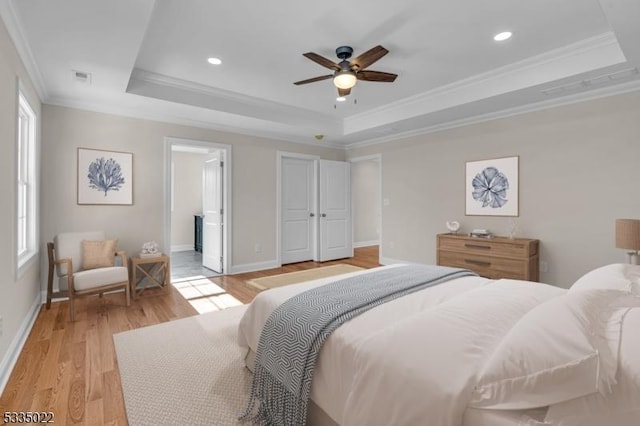 bedroom featuring ensuite bathroom, ceiling fan, a raised ceiling, crown molding, and light hardwood / wood-style flooring