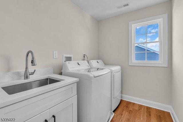 laundry area featuring sink, washing machine and dryer, cabinets, and light wood-type flooring