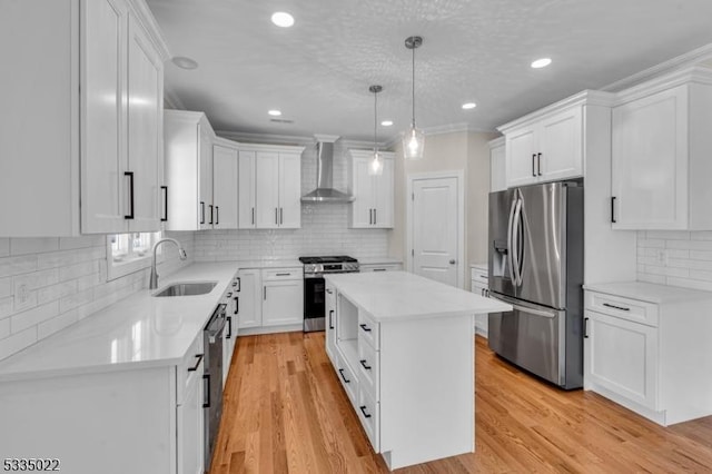 kitchen featuring sink, appliances with stainless steel finishes, a kitchen island, wall chimney range hood, and white cabinets