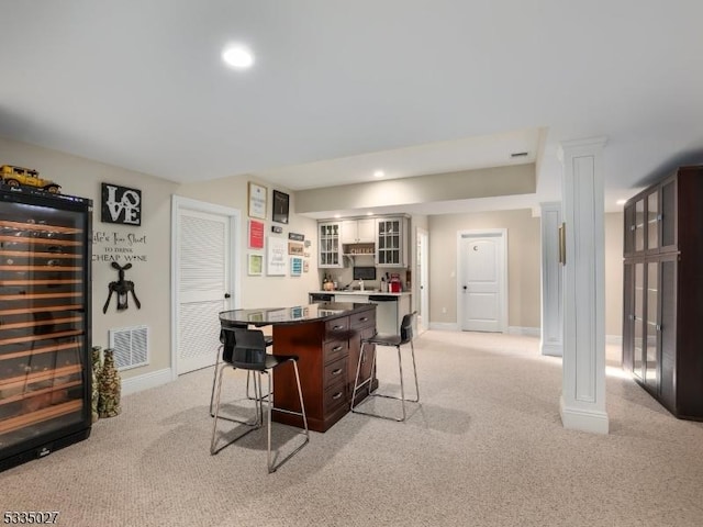 interior space featuring beverage cooler, a kitchen bar, a center island, dark brown cabinetry, and light carpet