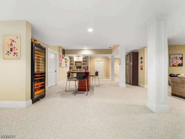 kitchen featuring beverage cooler, light carpet, a breakfast bar area, and ornate columns