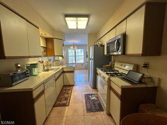 kitchen featuring sink, white appliances, cream cabinetry, and a chandelier