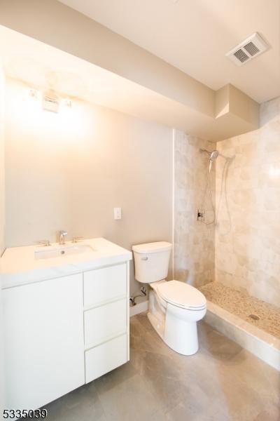 bathroom featuring vanity, toilet, and a tile shower