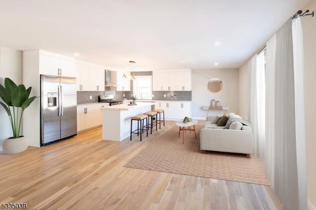 kitchen with stainless steel refrigerator with ice dispenser, a breakfast bar area, white cabinetry, a center island, and wall chimney range hood