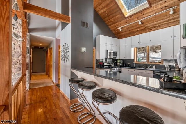 kitchen featuring a skylight, visible vents, white cabinets, a peninsula, and stainless steel appliances