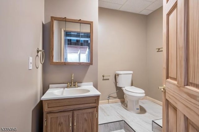 bathroom with toilet, a drop ceiling, vanity, and baseboards