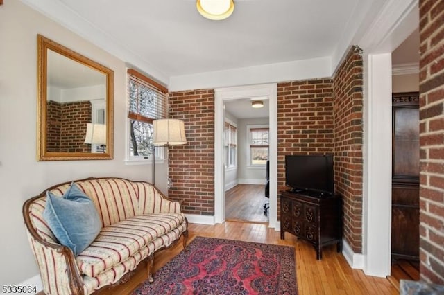 sitting room with light wood-style floors, baseboards, a healthy amount of sunlight, and brick wall