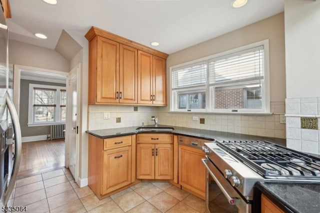 kitchen featuring tasteful backsplash, dark countertops, radiator heating unit, stainless steel appliances, and a sink