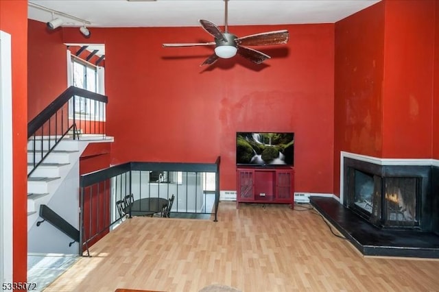 living room with wood finished floors, a multi sided fireplace, a ceiling fan, and track lighting