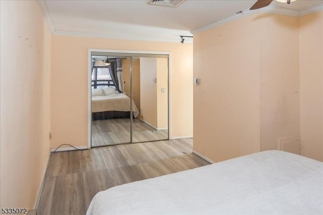 bedroom with a closet, crown molding, baseboards, and wood finished floors