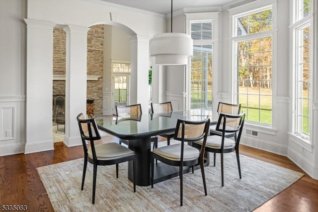 dining space with ornate columns, crown molding, a fireplace, and dark hardwood / wood-style flooring