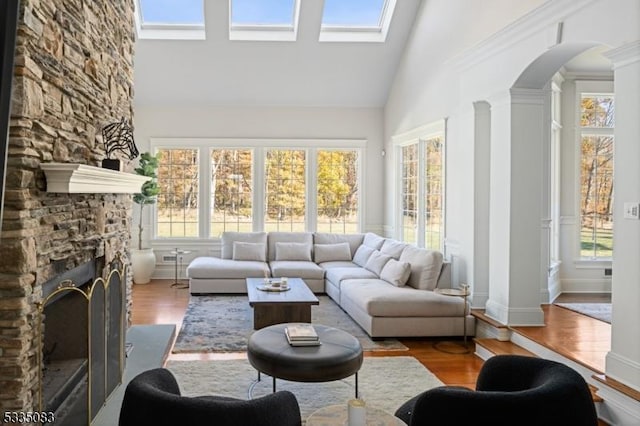 sunroom with lofted ceiling, a stone fireplace, and decorative columns