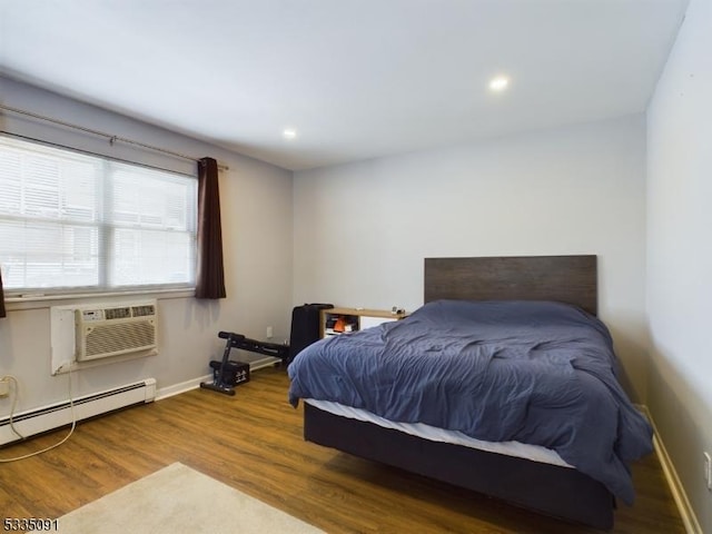 bedroom with baseboard heating, wood-type flooring, and a wall unit AC