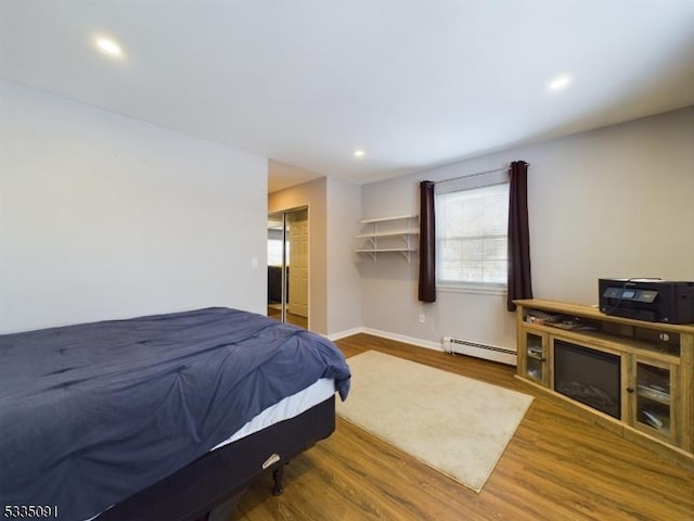 bedroom with hardwood / wood-style flooring, a closet, and a baseboard heating unit