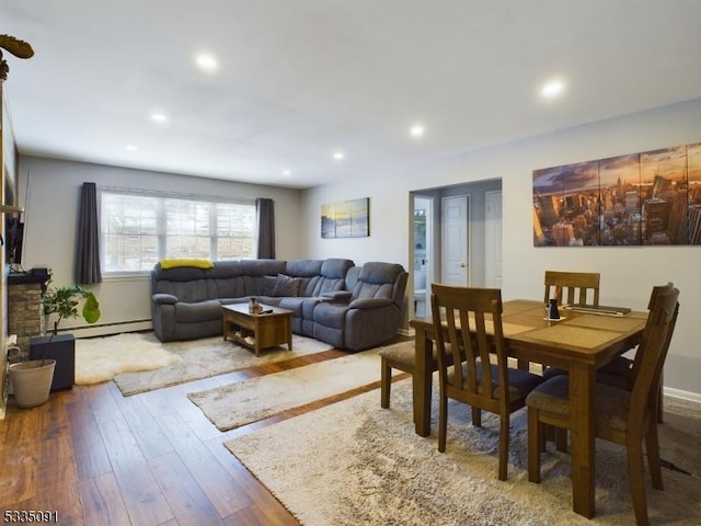 dining area with wood-type flooring, a baseboard heating unit, and a fireplace