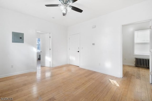 empty room featuring ceiling fan, electric panel, radiator, and light wood-type flooring