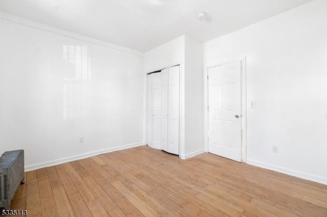 unfurnished bedroom featuring radiator, light hardwood / wood-style floors, and a closet