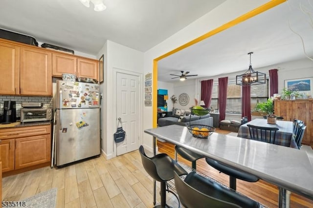 kitchen with light hardwood / wood-style flooring, stainless steel refrigerator, ceiling fan, decorative backsplash, and decorative light fixtures