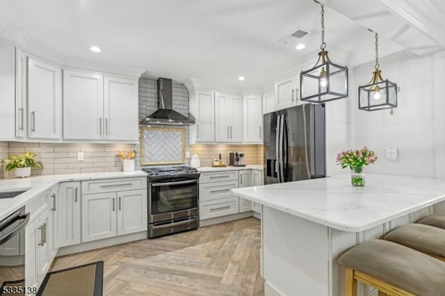 kitchen featuring pendant lighting, stainless steel appliances, white cabinets, a kitchen bar, and wall chimney exhaust hood