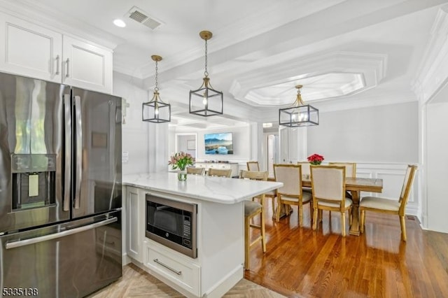 kitchen featuring stainless steel refrigerator with ice dispenser, white cabinetry, hanging light fixtures, black microwave, and ornamental molding