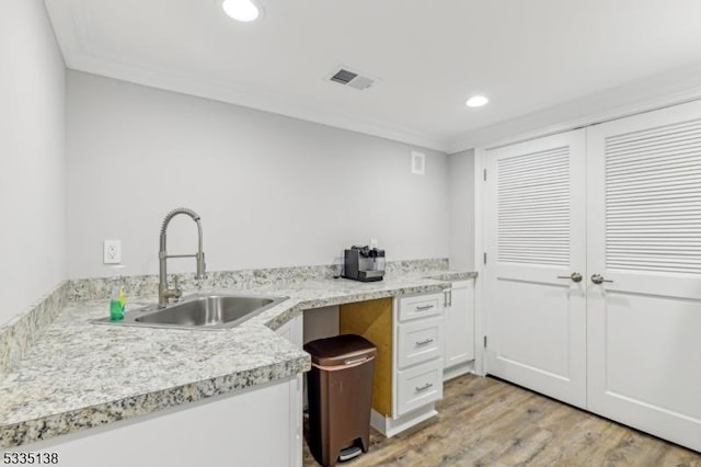 kitchen featuring sink, white cabinets, ornamental molding, light hardwood / wood-style floors, and light stone countertops