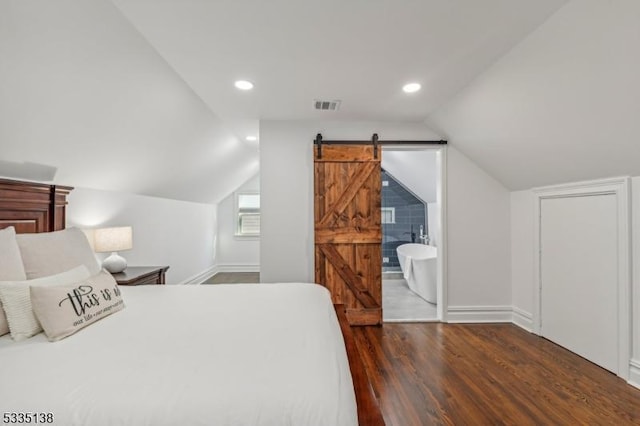 bedroom with dark hardwood / wood-style floors, a barn door, and vaulted ceiling