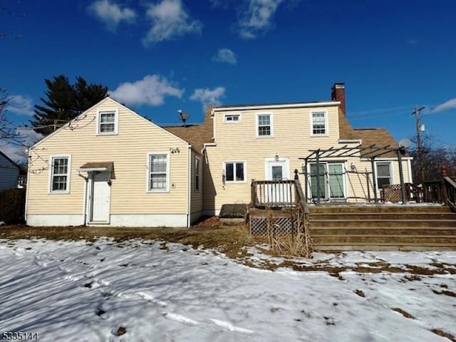 snow covered rear of property with a deck and a pergola