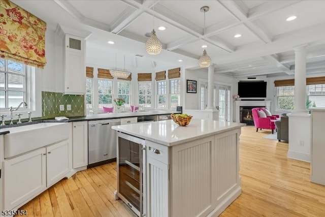 kitchen featuring wine cooler, light countertops, stainless steel dishwasher, open floor plan, and ornate columns