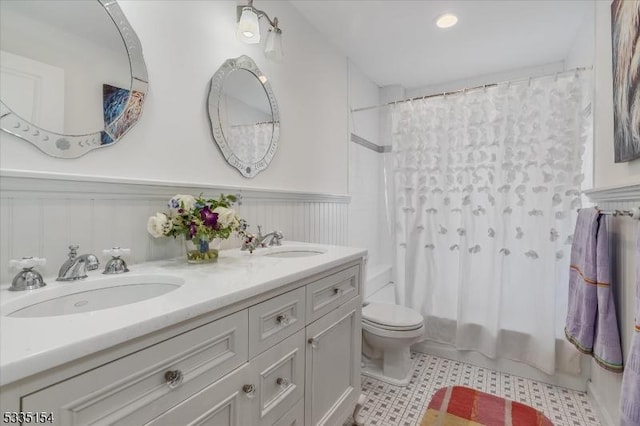 full bath with double vanity, toilet, a sink, and wainscoting