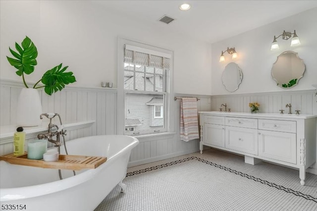 full bathroom with a freestanding tub, a wainscoted wall, visible vents, and double vanity