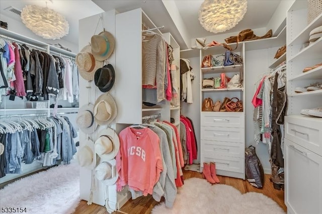 walk in closet with light wood-style flooring and a notable chandelier