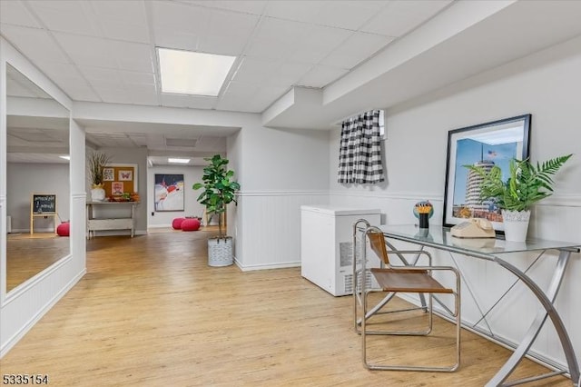 office with wainscoting, a drop ceiling, and light wood-style flooring