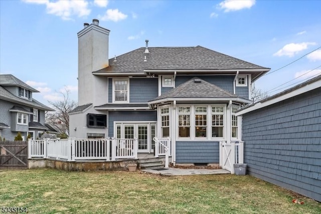 rear view of property with a shingled roof, a chimney, a lawn, and a wooden deck