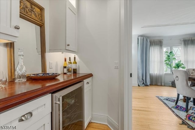 bar with beverage cooler, a bar, baseboards, and light wood-style floors