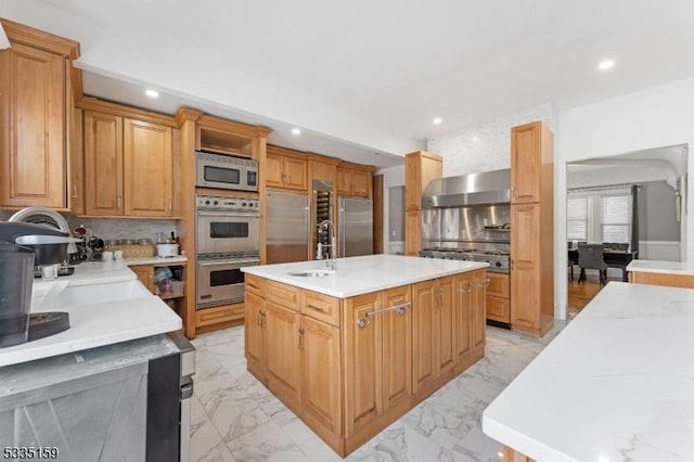 kitchen featuring tasteful backsplash, sink, a kitchen island with sink, stainless steel appliances, and wall chimney range hood