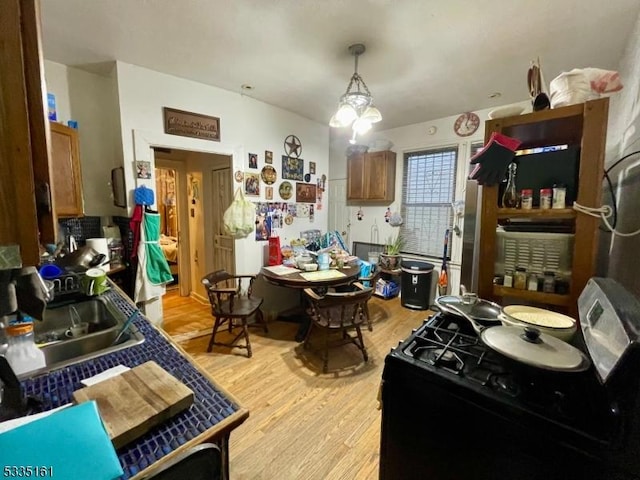 kitchen with range with gas stovetop, sink, light hardwood / wood-style floors, and hanging light fixtures