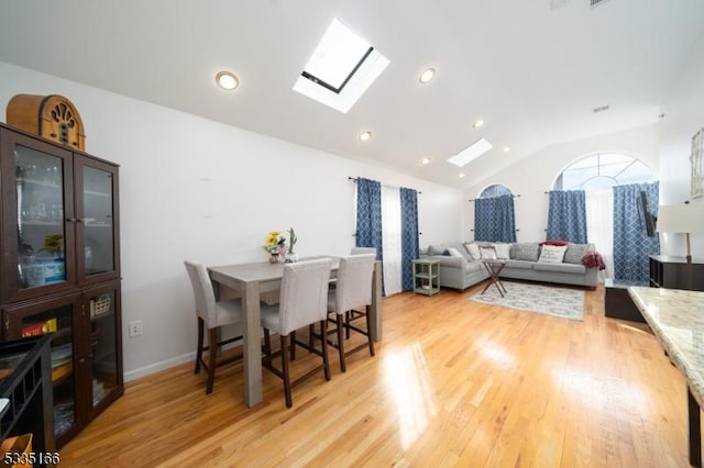 dining space with vaulted ceiling with skylight and light wood-type flooring