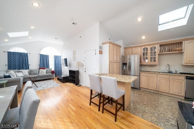 kitchen featuring sink, appliances with stainless steel finishes, a center island, vaulted ceiling with skylight, and light brown cabinets