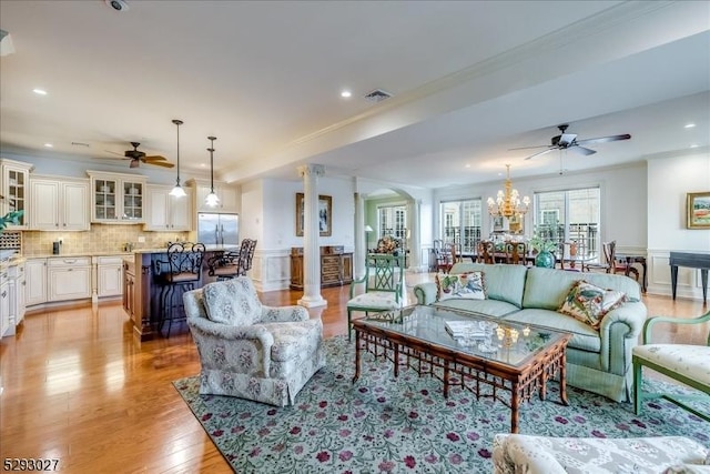 living room featuring ceiling fan with notable chandelier, ornamental molding, light hardwood / wood-style floors, and decorative columns