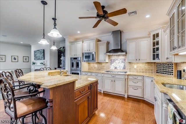 kitchen with wall chimney exhaust hood, a center island with sink, appliances with stainless steel finishes, a kitchen breakfast bar, and pendant lighting