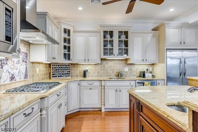 kitchen with wall chimney exhaust hood, white cabinetry, tasteful backsplash, stainless steel appliances, and light stone countertops