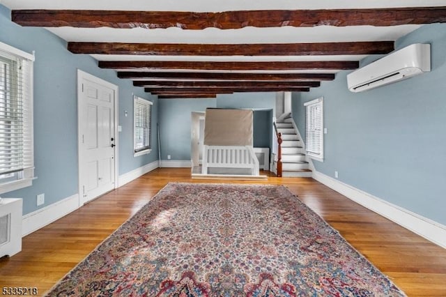 entrance foyer featuring beamed ceiling, a wall mounted AC, and light wood-type flooring