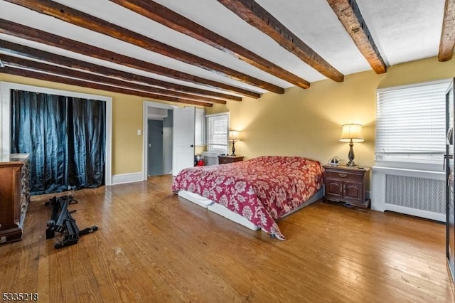 bedroom with beamed ceiling, wood-type flooring, and radiator heating unit