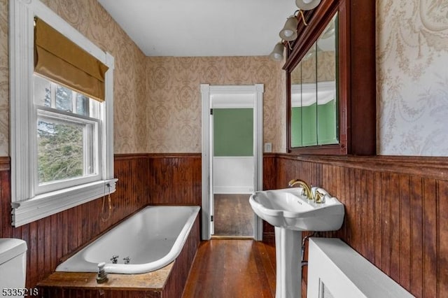 bathroom featuring a washtub, wood-type flooring, wooden walls, and toilet