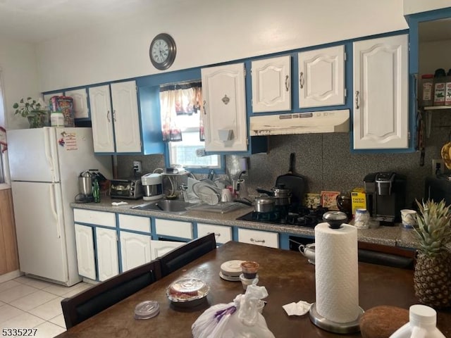 kitchen with light tile patterned flooring, black stovetop, white fridge, and white cabinets