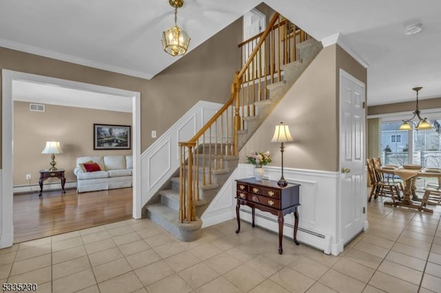 stairs featuring a baseboard heating unit, ornamental molding, tile patterned floors, and a chandelier