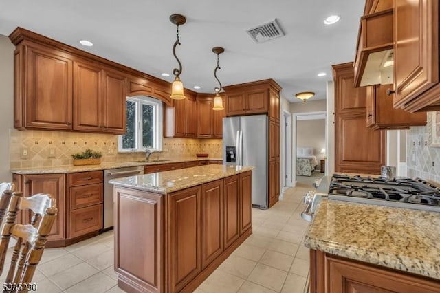 kitchen featuring sink, light stone counters, a center island, hanging light fixtures, and appliances with stainless steel finishes