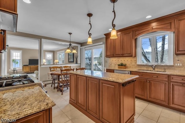 kitchen with sink, light stone counters, decorative light fixtures, a kitchen island, and decorative backsplash