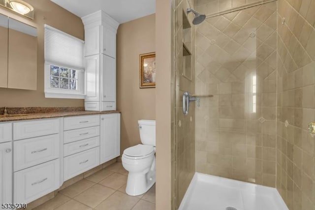 bathroom with tile patterned flooring, vanity, a tile shower, and toilet